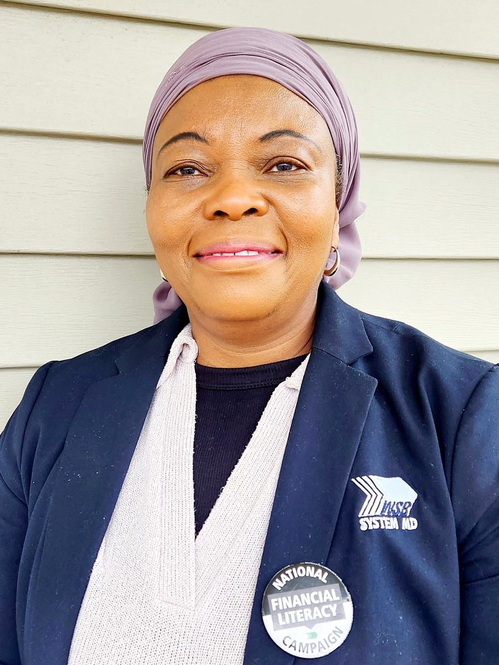 Rasheedatu Nyei, licensed financial advisor, standing outdoors in a navy blazer with a National Financial Literacy Campaign pin